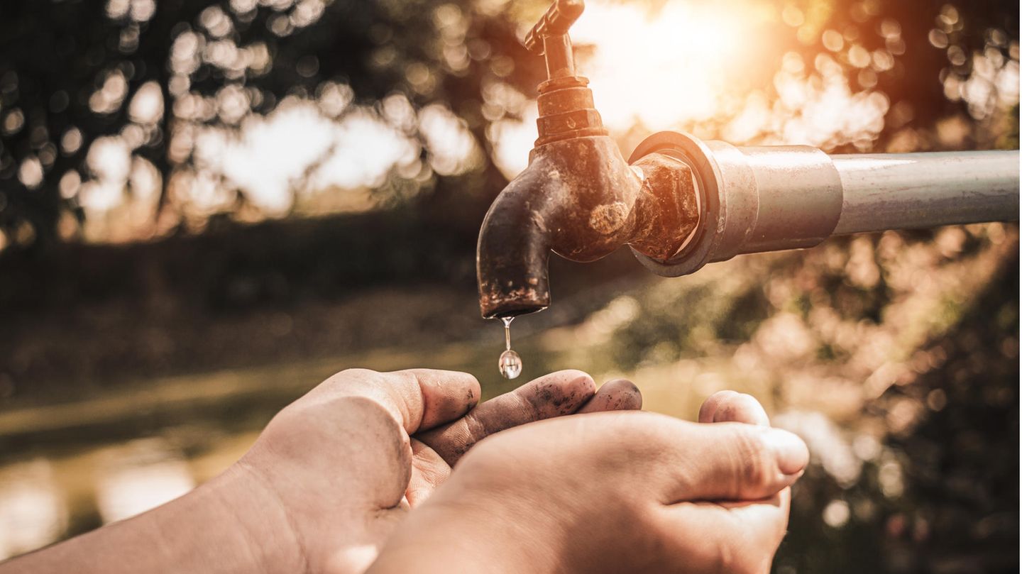 Hände unter einem Wasserhahn im Garten