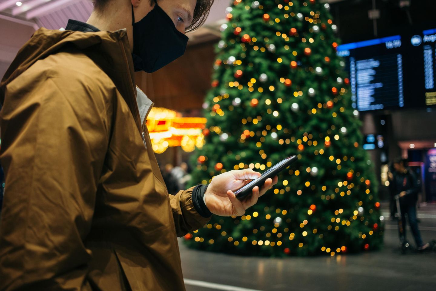 Mann blick am Bahnhof an Weihnachten auf sein Smartphone
