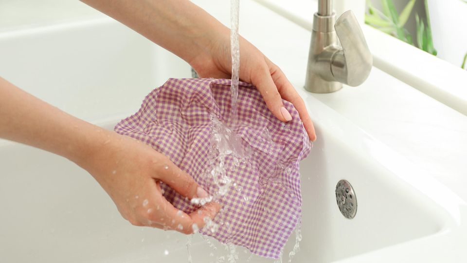 Eine Frau wäscht in der Küche ein Bienenwachstuch unter fließendem Wasser ab