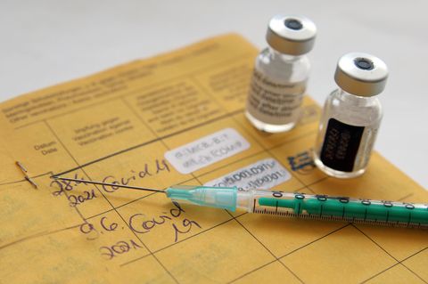 Spritze und Impfstoff gegen Corona liegen auf einem Impfausweis
