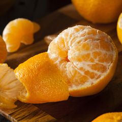Geschälte Mandarine liegt auf einem Holzbrett mit Resten der Schale