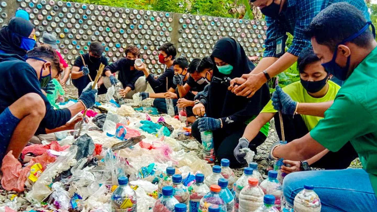 Die Dorfbewohnerinnen und -bewohner sor­tieren und trocknen den Plastikabfall. Dann stopfen sie ihn in Flaschen, bis diese proppenvoll und schwer wie Ziegelsteine sind.