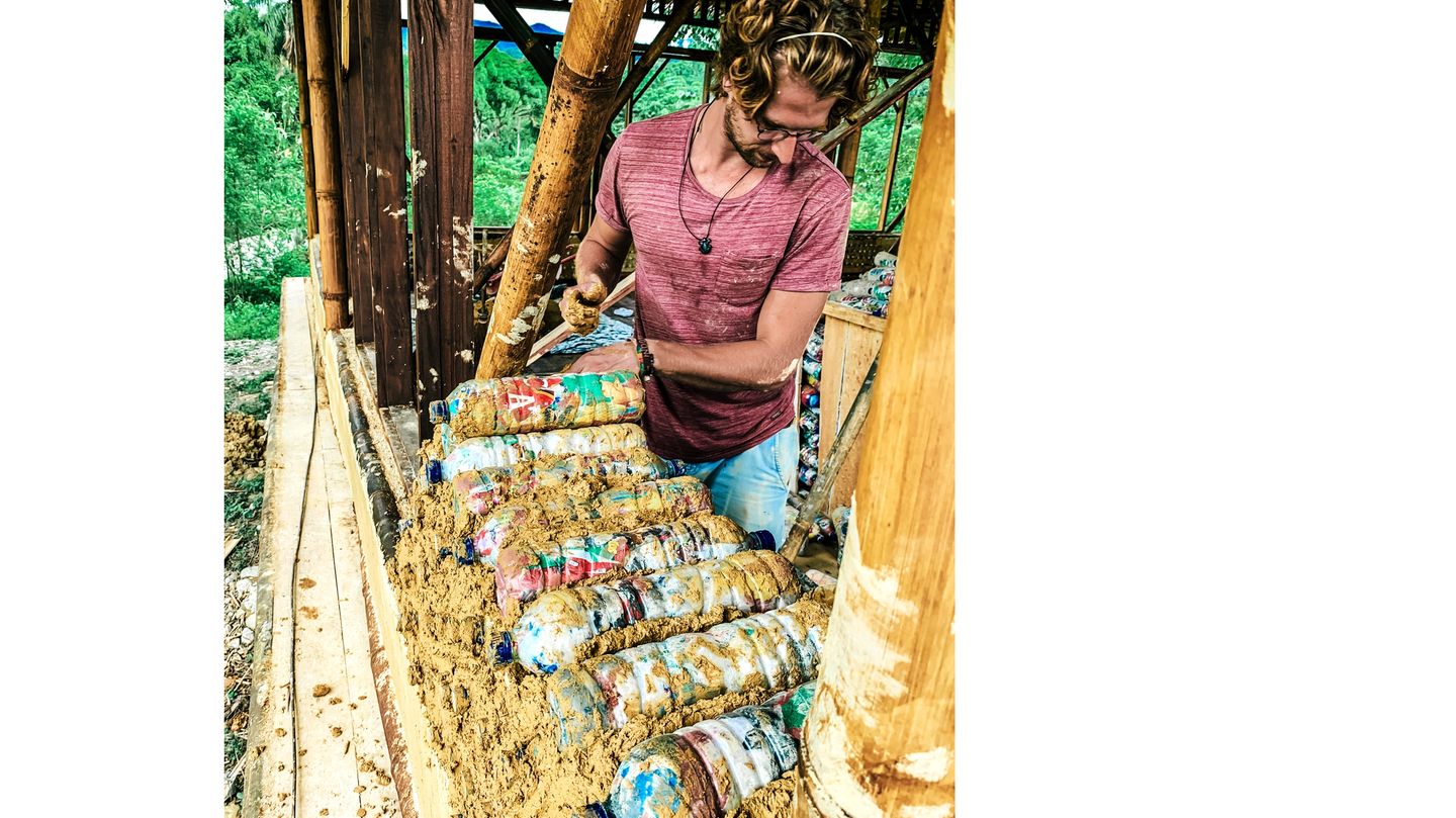 Stein auf Stein – oder eher: Flasche auf Flasche – mauert dieser freiwillige Helfer eine Wand. »Ecobricks« nennen sie den Upcycling- Baustoff, »Ökoziegel«.