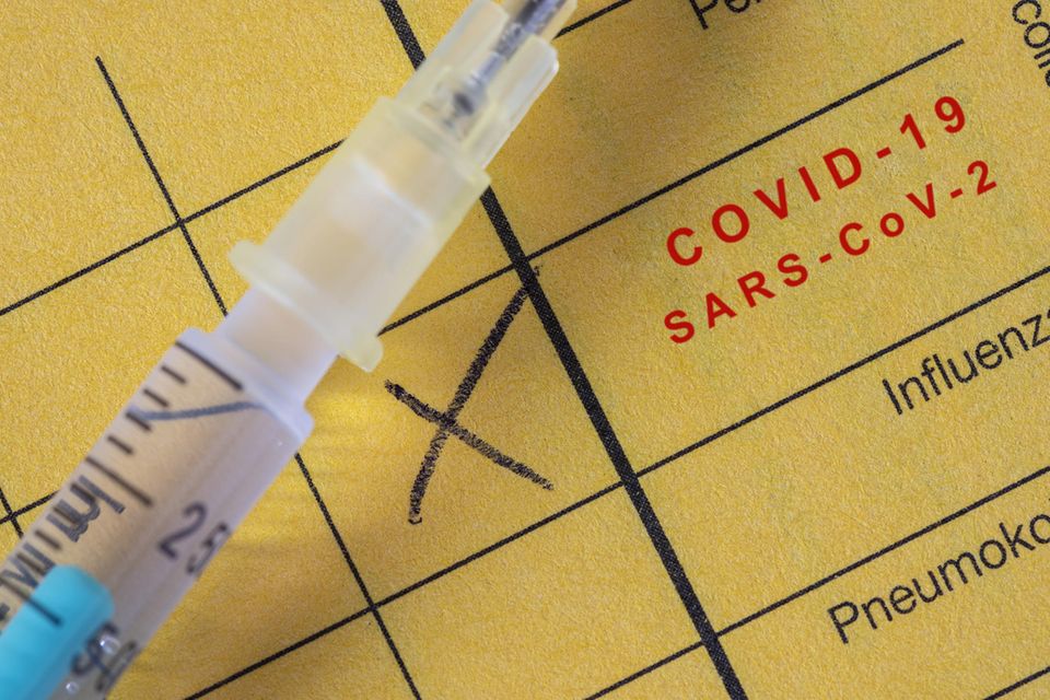Spritze liegt auf einem Impfausweis mit eingetragener Covid-Impfung