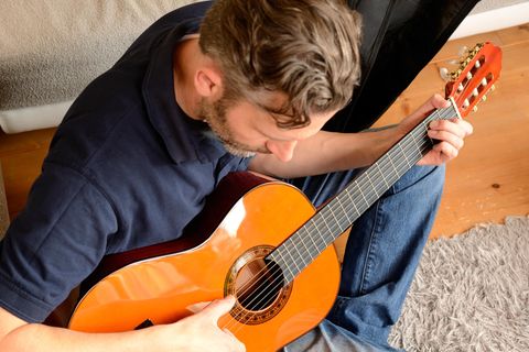 Mann sitzt im Wohnzimmer und spielt auf einer Konzertgitarre