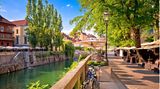 Flusspromenade in Ljubljana mit Cafés unter Bäumen