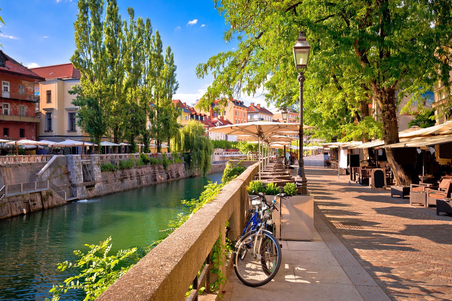 Flusspromenade in Ljubljana mit Cafés unter Bäumen