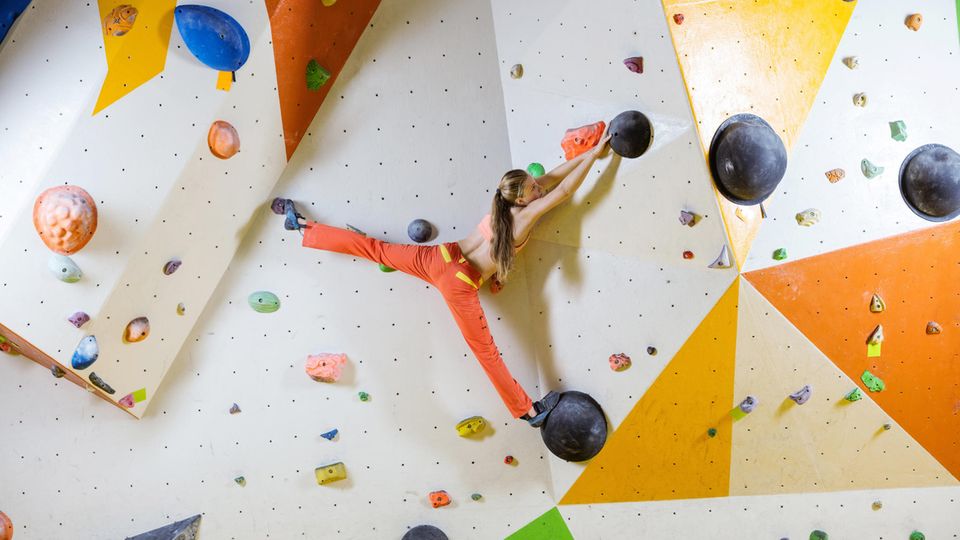 Eine junge Frau steht fast im Spagat auf zwei Tritten an der Boulderwand. Eine junge Frau steht fast im Spagat auf zwei Tritten an der Boulderwand.