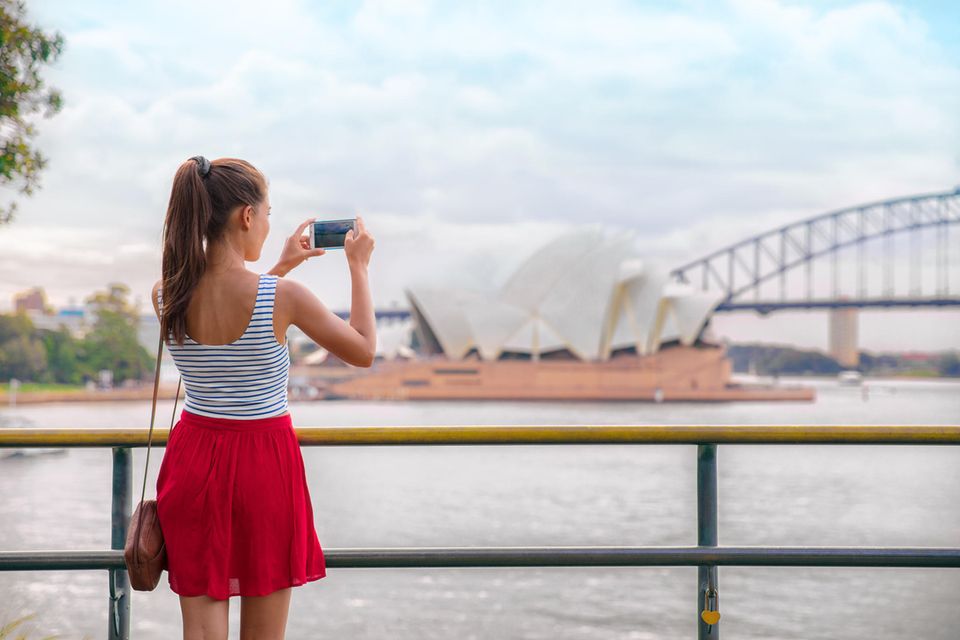 Junge Frau fotografiert die Oper von Sydney mit dem Handy
