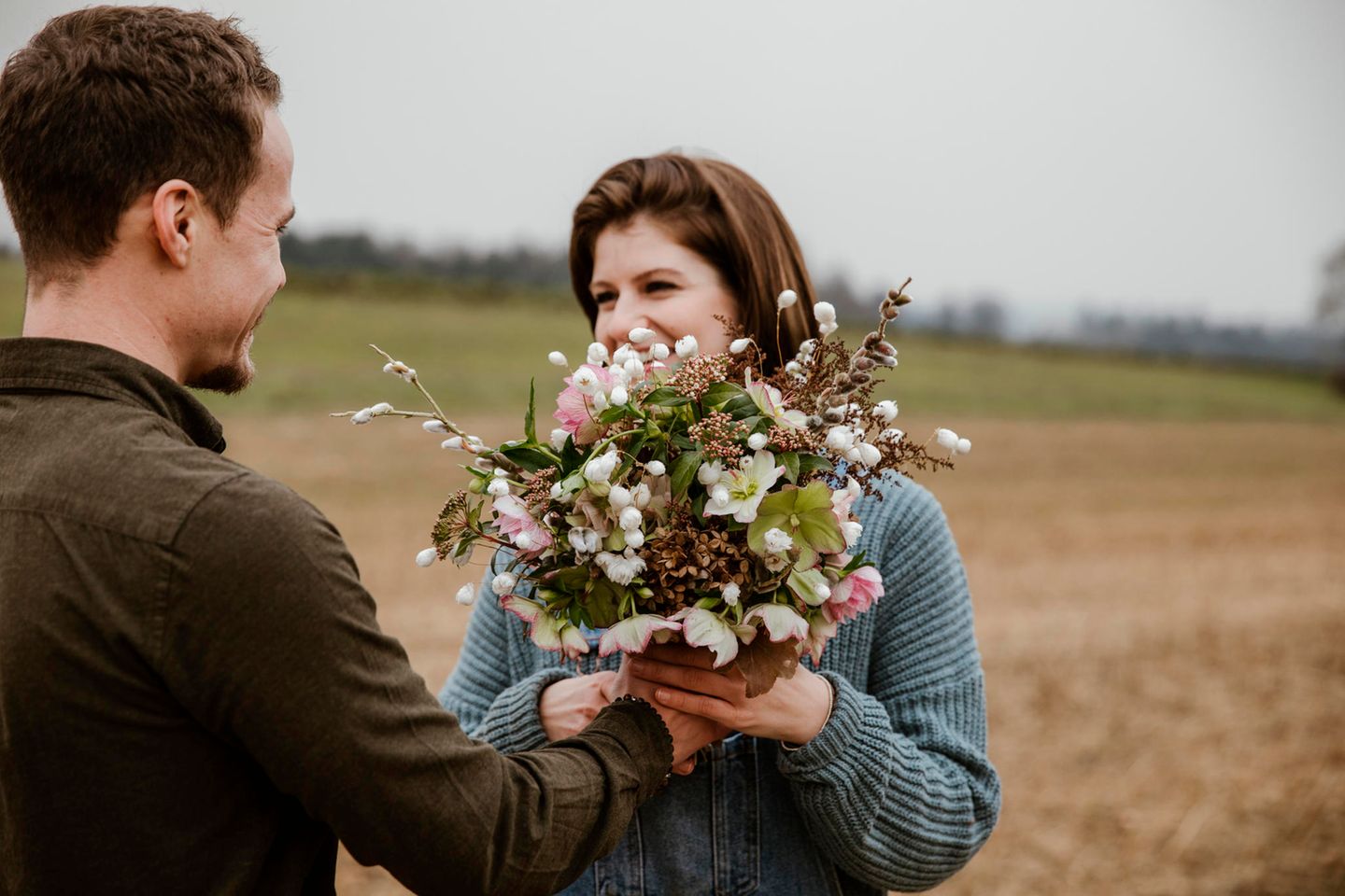 Mann überreicht Frau einen Blumenstrauß mit Christrosen und Weidenkätzchen
