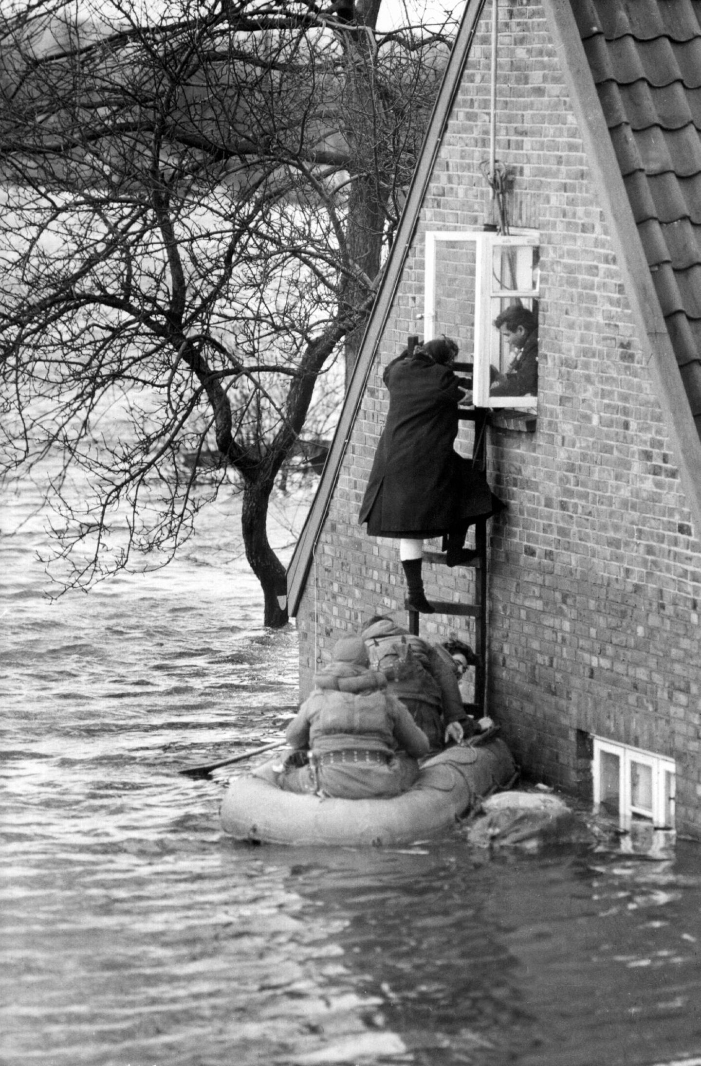Menschen flüchten über Leitern aus einem gefluteten Haus