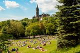 View of Kelvingrove Park full of people enjoying the Scottish summer with main building of Glasgow University on the top of hill