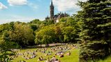 View of Kelvingrove Park full of people enjoying the Scottish summer with main building of Glasgow University on the top of hill