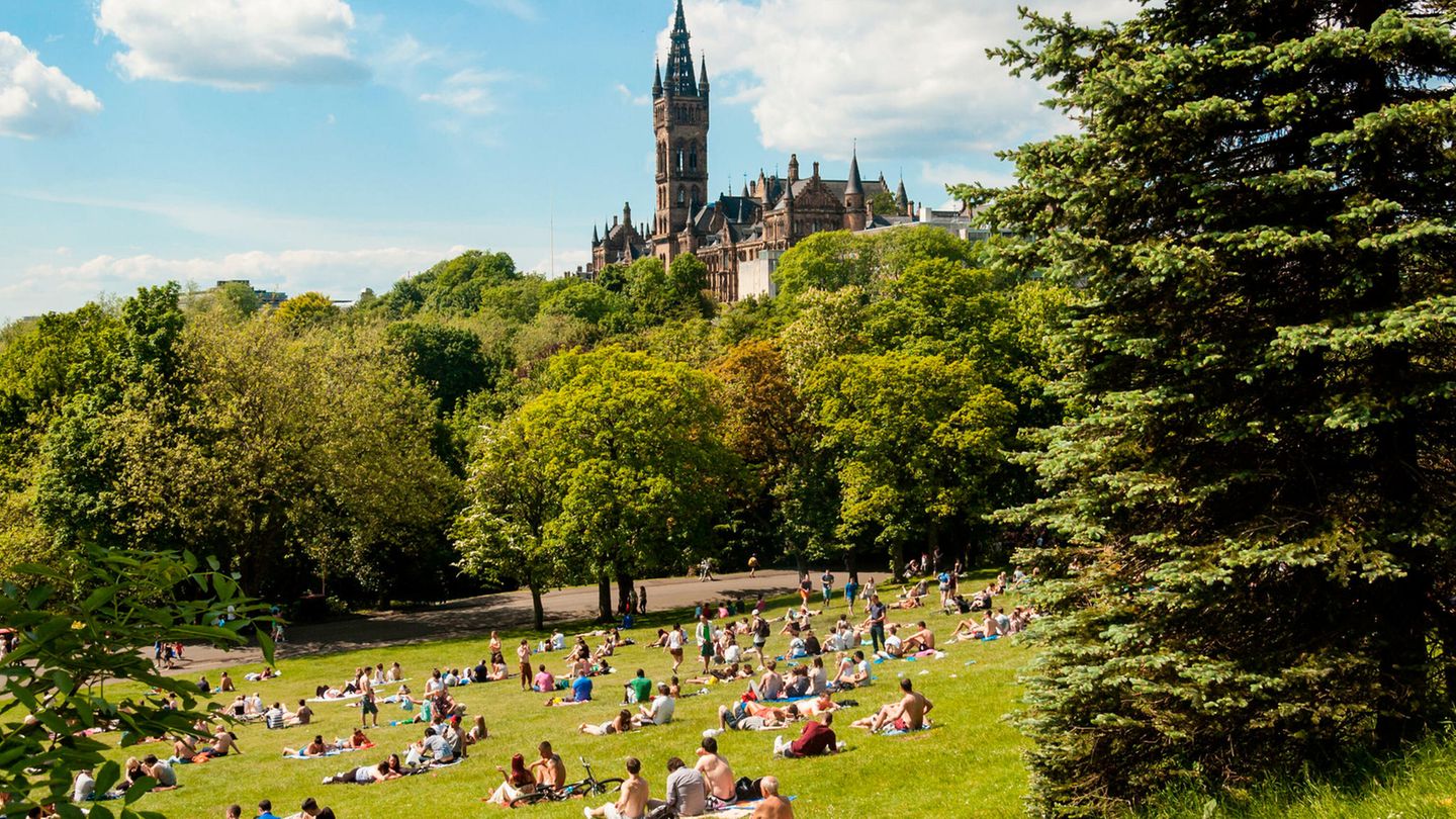 View of Kelvingrove Park full of people enjoying the Scottish summer with main building of Glasgow University on the top of hill