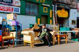 Eine bunt gekleidete Frau sitzt auf einem alten Sofa im Barras Market