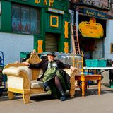 Eine bunt gekleidete Frau sitzt auf einem alten Sofa im Barras Market