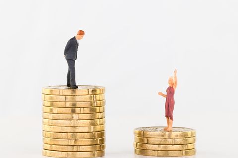 Zwei Miniaturfiguren stehen auf unterschiedlich hohen Münzstapeln