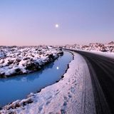 Ein schmaler Fluss fließt neben einer Straße entlang. Der Himmel ist blau-rosa gefärbt