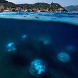 Image Name: Nemo's Garden 10  Photographer Name: Giacomo d'Orlando  Year: 2022  Image Description: <p>Nemo's Garden seen from the water’s surface. The biospheres are located 40 metres off the Noli shore – a small village on the Ligurian coast. They are constructed 6-12 meter below the surface of the water, to enable the plants to draw the necessary source of light for their development. In the centre stands the tree of life which represents the core of the experiment: the possibility of growing terrestrial plants underwater.</p>  Series Name: Nemo's Garden  Series Description: According to the Intergovernmental Panel on Climate Change (IPCC), the desertification brought by climate change in recent years has already extensively reduced agricultural productivity in many regions of the world. Agriculture represents 70% of freshwater use around the globe and with the world’s population projected to increase to 10 billion by the end of the century, it has become imperative to find alternative and ecologically sustainable methods of cultivation. Nemo’s Garden – the world’s first underwater greenhouse – offers a possible solution. This completely self-sustainable project explores an alternative farming system that could be implemented in areas where environmental or geo-morphological conditions make the growth of plants almost impossible. The encouraging results of the last few years, where more than 40 different species of plants have been successfully cultivated, gives hope that a sustainable agricultural system has been developed to help tackle the new challenges brought by climate change.