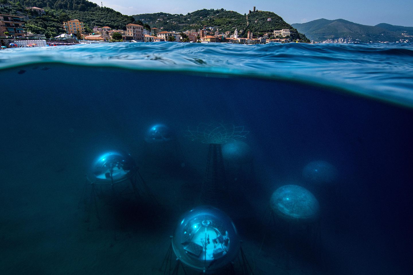 Image Name: Nemo's Garden 10  Photographer Name: Giacomo d'Orlando  Year: 2022  Image Description: <p>Nemo's Garden seen from the water’s surface. The biospheres are located 40 metres off the Noli shore – a small village on the Ligurian coast. They are constructed 6-12 meter below the surface of the water, to enable the plants to draw the necessary source of light for their development. In the centre stands the tree of life which represents the core of the experiment: the possibility of growing terrestrial plants underwater.</p>  Series Name: Nemo's Garden  Series Description: According to the Intergovernmental Panel on Climate Change (IPCC), the desertification brought by climate change in recent years has already extensively reduced agricultural productivity in many regions of the world. Agriculture represents 70% of freshwater use around the globe and with the world’s population projected to increase to 10 billion by the end of the century, it has become imperative to find alternative and ecologically sustainable methods of cultivation. Nemo’s Garden – the world’s first underwater greenhouse – offers a possible solution. This completely self-sustainable project explores an alternative farming system that could be implemented in areas where environmental or geo-morphological conditions make the growth of plants almost impossible. The encouraging results of the last few years, where more than 40 different species of plants have been successfully cultivated, gives hope that a sustainable agricultural system has been developed to help tackle the new challenges brought by climate change.