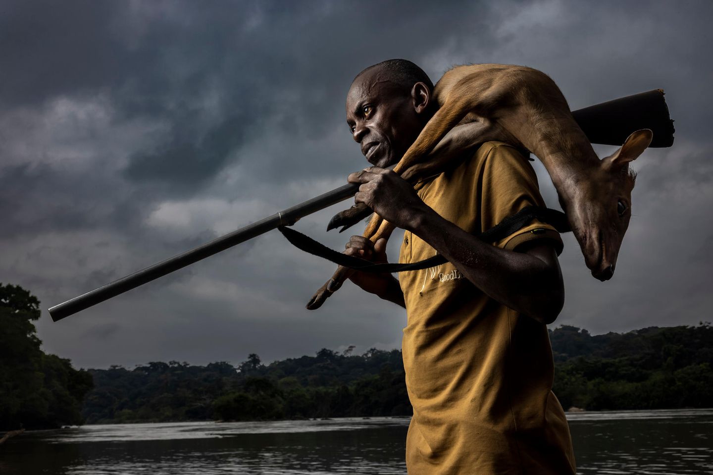 Image Name: Hunters 1  Photographer Name: Brent Stirton  Year: 2022  Image Description: <p>DOUME VILLAGE, LASTOURSVILLE, GABON, 29 JUNE 2021: Expert bushmeat hunter Nkani Mbou Mboudin is seen with an antelope he just shot hunting in the forest around his village. This village survives on fishing and bushmeat. Gabon has a sustainable bushmeat culture, largely because of its small population and large protected habitats.</p>  Series Name: Bushmeat Hunters  Series Description: This is a series of bushmeat hunter portraits taken in Guyana, Gabon, the Democratic Republic of Congo and the Republic of Congo. These men are seen in an age-old act, bringing animals they have hunted back to their villages. Some of these men are hunting for other, wealthier men who have employed them, others are hunting for their families. In all cases, very little of what they hunted was consumed in the village. Bushmeat commands a high price, which increases as it gets to major cities. These days, hunting of this kind is almost always about an economy of supply and demand.