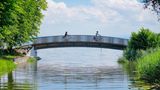 Zwei Fahrradfahrer überqueren die Brücke über den Bach Aach bei der Mündung in den Bodensee