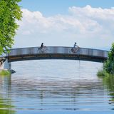 Zwei Fahrradfahrer überqueren die Brücke über den Bach Aach bei der Mündung in den Bodensee