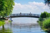 Zwei Fahrradfahrer überqueren die Brücke über den Bach Aach bei der Mündung in den Bodensee