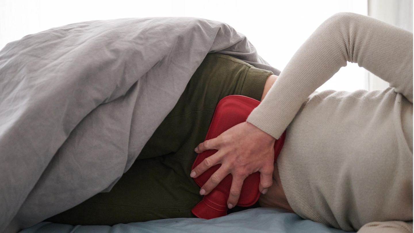 Eine Frau hält sich eine Wärmflasche an den Unterbauch, während sie im Bett liegt