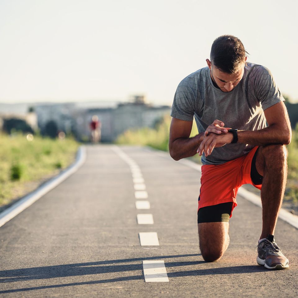 Pulsuhr im Einsatz: Ein Mann in sportlicher Kleidung macht sich bereit für seinen Lauf und liest etwas von seiner Pulsuhr ab.