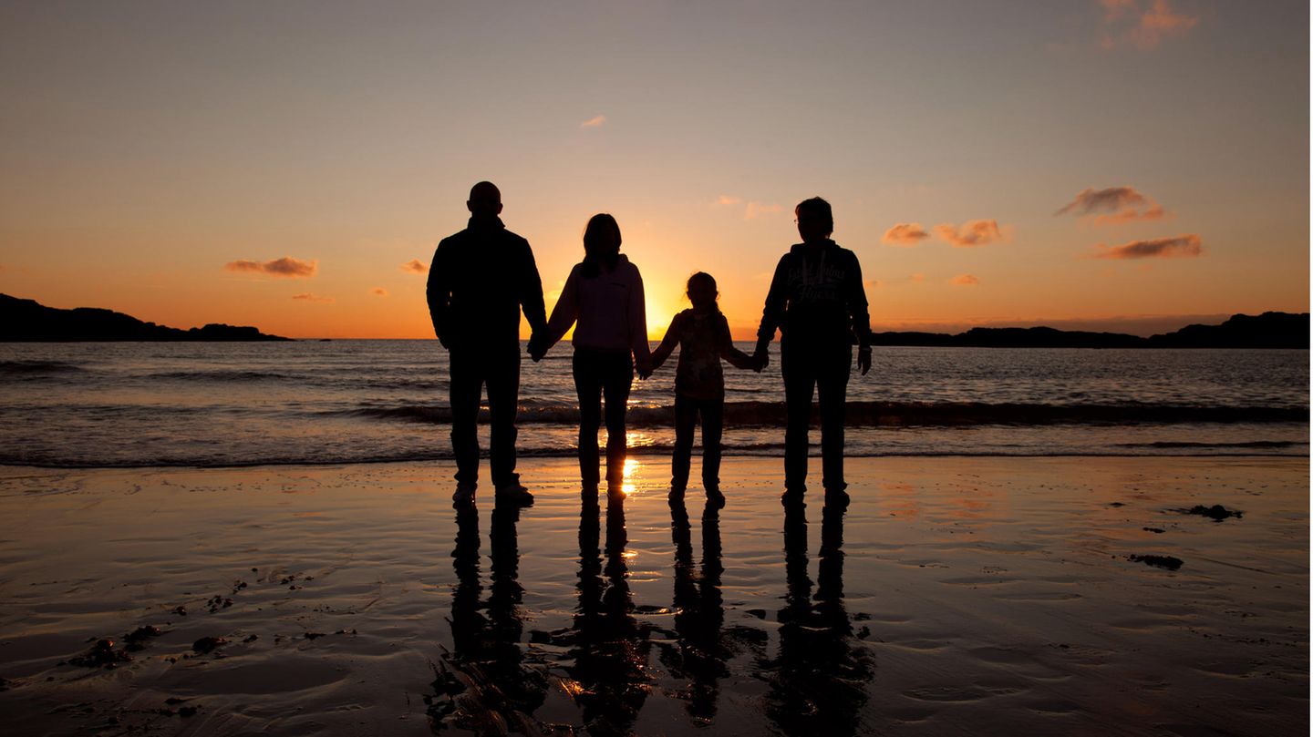 Familie mit zwei Kindern steht zum Sonnenuntergang am Strand