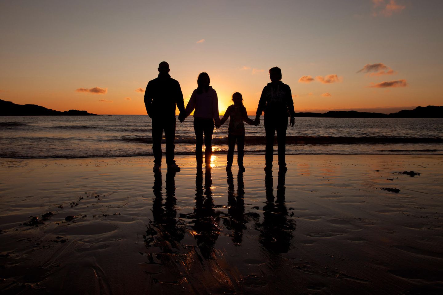 Familie mit zwei Kindern steht zum Sonnenuntergang am Strand