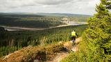 Mountainbiker auf einem Trail mit Blick auf Wälder und See