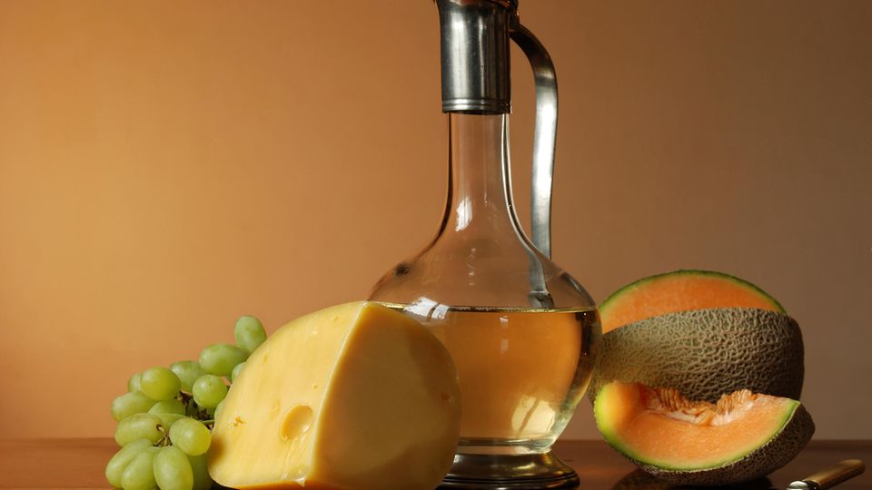 Einige Lebensmittel die Erythrit enthalten stehen auf einem Tisch: Weintrauben, Käse, Melone und Weißwein.