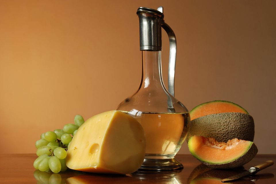 Einige Lebensmittel die Erythrit enthalten stehen auf einem Tisch: Weintrauben, Käse, Melone und Weißwein.