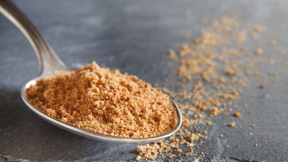 Ein Löffel mit braunem, groben Kokosblütenzucker.