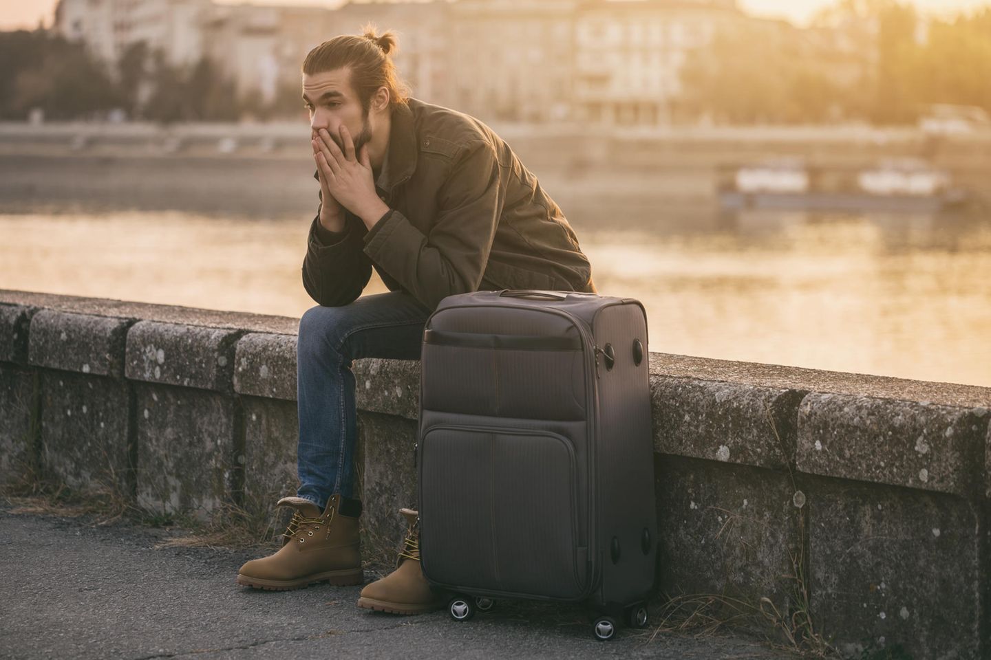 Verzweifelter Mann sitzt auf einer Brücke mit seinem Koffer