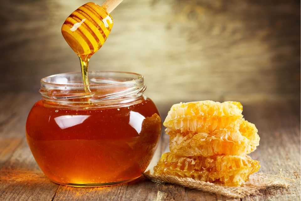 Ein Glas Honig mit Honigwaben daneben.