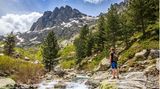 Wanderer steht an einem wilden Fluss mit Blick auf Bergspitzen