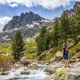 Wanderer steht an einem wilden Fluss mit Blick auf Bergspitzen
