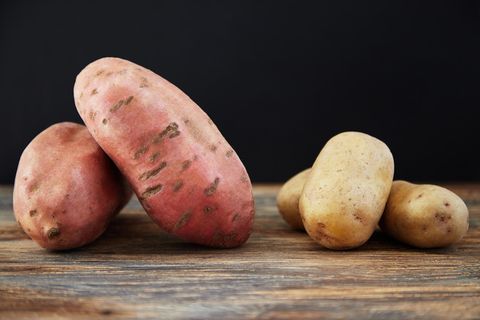 Süßkartoffeln und gewöhnliche Kartoffeln auf einem Holzbrett