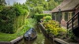 Kleines Ruderboot liegt auf einem Kanal an einem Reetdachhaus