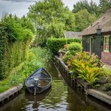 Kleines Ruderboot liegt auf einem Kanal an einem Reetdachhaus