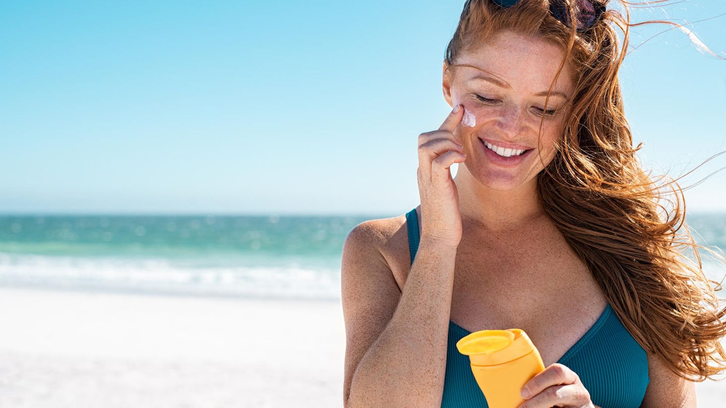 Eine rothaarige Frau cremt sich am Strand mit Sonnencreme ein