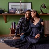 Die Fotografin und ihr Mann sitzen auf dem Boden und schauen zur Seite. Neben ihnen auf dem Boden liegen Fotos verstreut