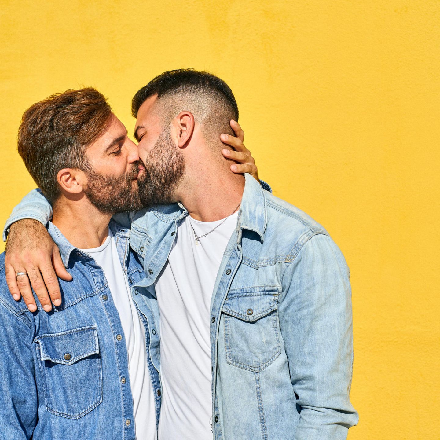 Schwules Pärchen küsst sich vor einer gelben Wand