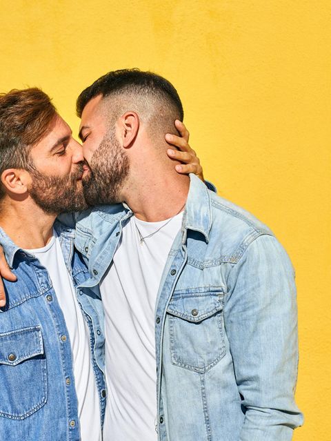 Schwules Pärchen küsst sich vor einer gelben Wand