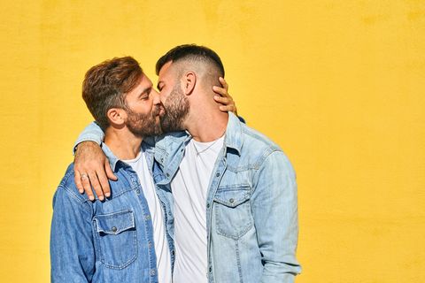 Schwules Pärchen küsst sich vor einer gelben Wand