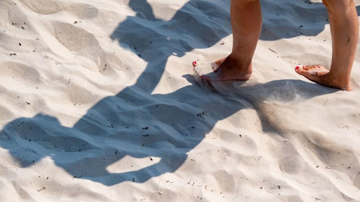 Eine Frau geht mit nackten Füßen durch den warmen Sand