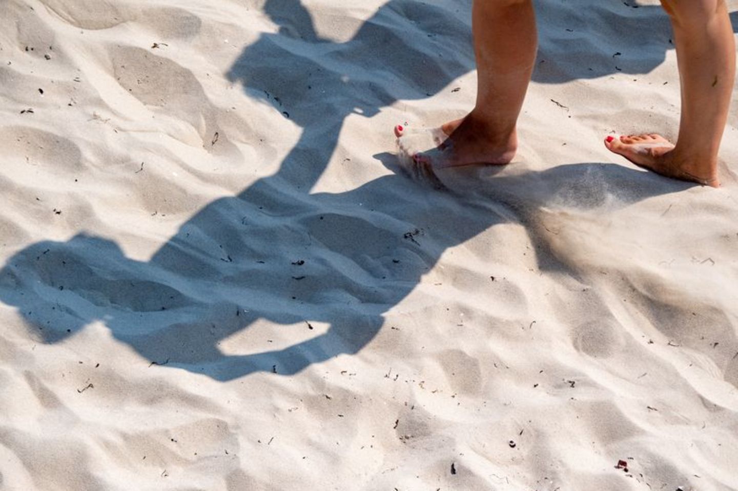 Eine Frau geht mit nackten Füßen durch den warmen Sand